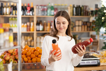 European teenage girl took various varieties of juices from shelf, chooses fruit drink for dinner...