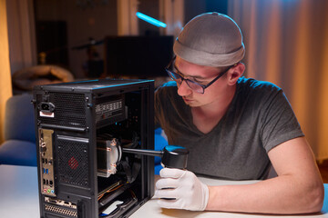A man cleans a computer case with a vacuum in a bright room, stressing workspace tidiness