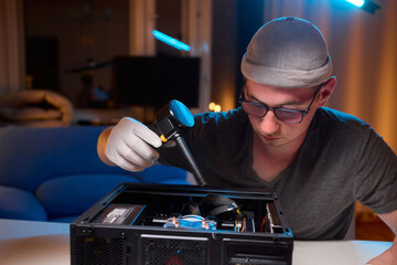 A man cleans a computer case with a vacuum in a bright room, stressing workspace tidiness