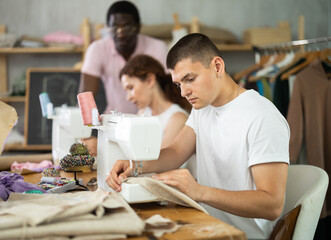 Focused young guy working on stitching machine during lesson at sewing class