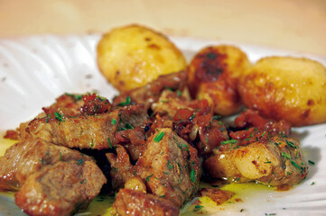 Juicy fried pork meat with roasted potatoes and herbs on white plate