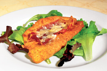 Breaded cutlet with bacon and cheese resting on a bed of lettuce