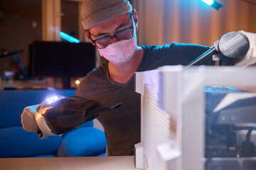 A man cleans a computer case with a vacuum in a bright room, stressing workspace tidiness