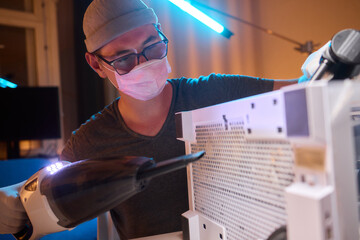 A man cleans a computer case with a vacuum in a bright room, stressing workspace tidiness