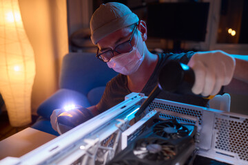 A man cleans a computer case with a vacuum in a bright room, stressing workspace tidiness