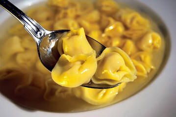 Spoon lifting tortellini from a bowl of broth