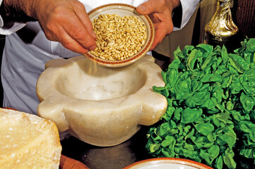 Chef pouring pine nuts into marble mortar for pesto sauce preparation