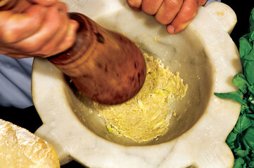 Chef crushing ingredients in mortar with pestle preparing pesto sauce