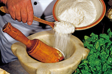 Chef adding grated cheese in marble mortar with pestle and basil for pesto sauce