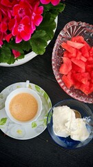 Top view of coffee with ice cream, watermelon slices and blooming pink flowers on black wooden table