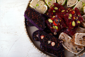 Sliced ​​Turkish delight assortment with cream filling, pistachio, almond, hazelnut, figs and cranberry on a ceramic plate on a white table. Local name: fistikli fitil lokum