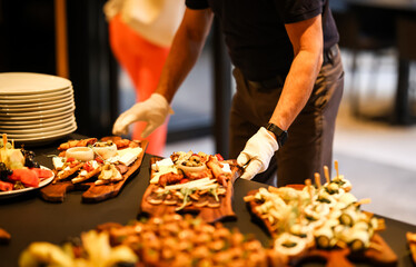 Caterer in white gloves arranging gourmet appetizer boards with cheeses, meats, and vegetables for...