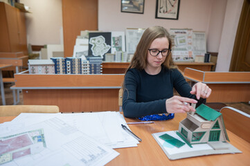 Caucasian young woman making a model of a building. Student of the construction university. 