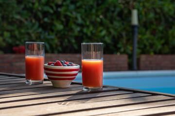 Healthy snack of fresh berries and juice on a wooden table in a garden by the pool