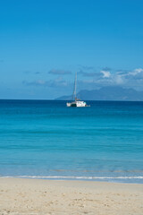 Fototapeta premium Beautiful beach of Beau Vallon, docking yacht, transparent and turquoise water, with silhouette island at the back, Mahe, Seychelles 