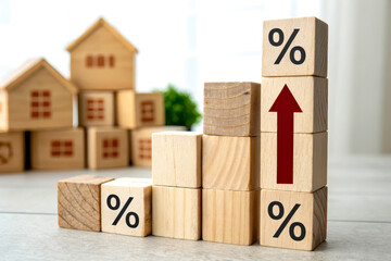 Wooden blocks with percentage signs and an upward arrow symbolize increasing mortgage rates, with small wooden house models blurred in the background.