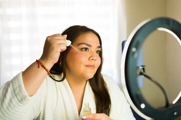 Latin beauty influencer applying serum on her face while recording a video