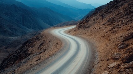 A beautifully winding dirt road curving through rugged mountains, inviting the viewer on a journey into the heart of nature's majestic landscape and adventurous spirit.