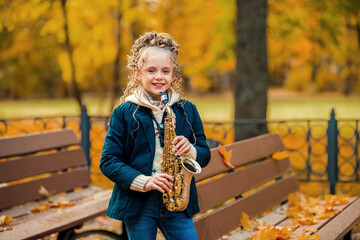 Young girl standing with saxophone in autumn park.