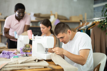 Attentive young male student of dressmaking courses working with sewing machine in workshop