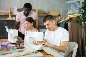 Focused young guy working on stitching machine during lesson at sewing class