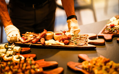 Caterer in white gloves arranging a gourmet appetizer board with meats, cheeses, sauces, and...