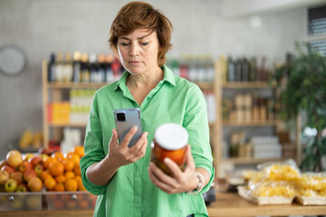Checking expiration date of canned food - female shopper scans QR code on label of pickled tomatoes...