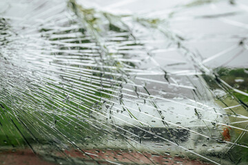 A cracked car windshield seen from the inside, with raindrops and a blurred outdoor scene including...