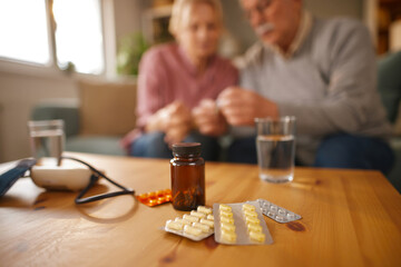 An elderly couple is sitting indoors, presumably in their home, sorting out pills and discussing...