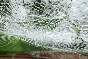 A cracked car windshield seen from the inside, with raindrops and a blurred outdoor scene including...
