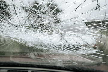 A cracked car windshield seen from the inside, with raindrops and a blurred outdoor scene including...
