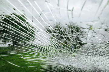 A cracked car windshield seen from the inside, with raindrops and a blurred outdoor scene including...
