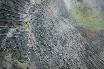 A cracked car windshield seen from the inside, with raindrops and a blurred outdoor scene including...