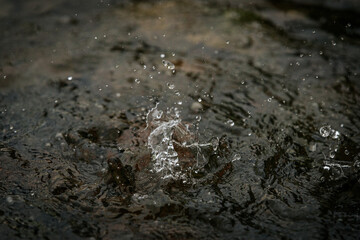 A close-up shot captures water droplets splashing and rippling on a dark surface, showing motion...