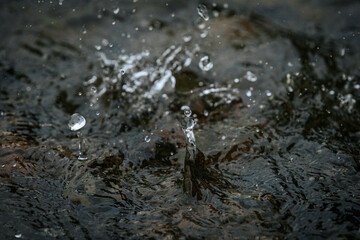 A close-up shot captures water droplets splashing and rippling on a dark surface, showing motion...