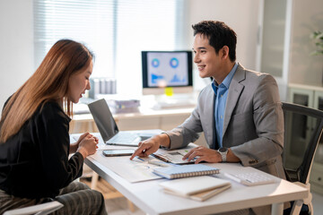 A man and a woman are sitting at a desk with a laptop and a monitor