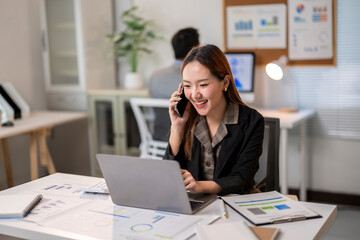 A woman is talking on her cell phone while sitting at a desk with a laptop