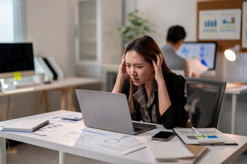 A woman is sitting at a desk with a laptop and a cell phone