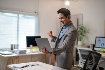 A man in a suit is holding a laptop and smiling