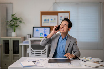 Naklejka premium A man in a suit is talking on his cell phone while sitting at a desk