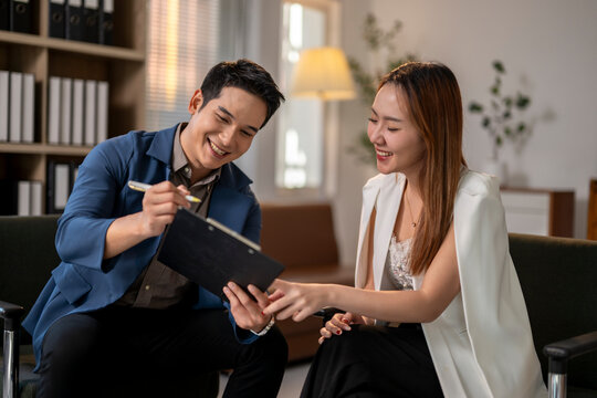 A man and a woman are sitting on a couch, looking at a clipboard - Powered by Adobe