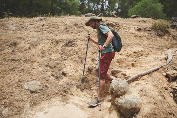 Man Hiking a Rugged Mountain Trail in Sunny Weather with Trekking Poles