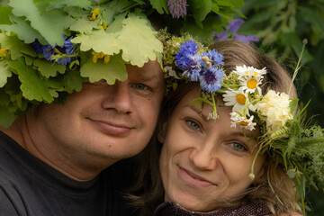 Close-up of a smiling couple wearing handmade floral crowns of oak leaves, daisies, and...