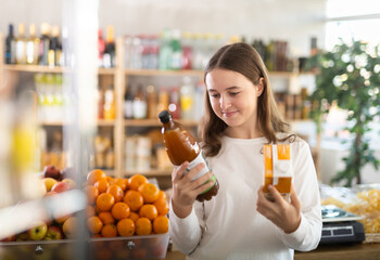European teenage girl took various varieties of juices from shelf, chooses fruit drink for dinner...