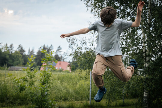 Boy mid-backflip on a trampoline in a garden setting, wearing casual clothes and Crocs, showcasing motion, agility, and outdoor fun.