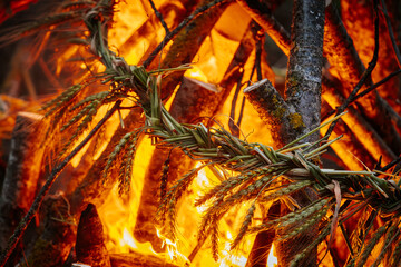 Close-up of a traditional braided wheat ornament burning in vivid orange flames, surrounded by...