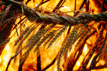Close-up of a traditional braided wheat ornament burning in vivid orange flames, surrounded by...