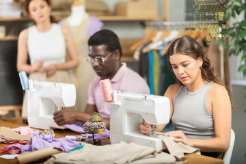 Attentive young female student of dressmaking courses working with sewing machine in workshop