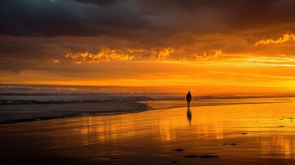 Sunset silhouette of a lone figure walking along the wet sand reflecting golden light