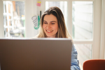 Beautiful young  woman working using computer laptop concentrated and smiling, she sitting at home, freelancer, girl have video call conference. Woman wear blue shirt, look happy.
